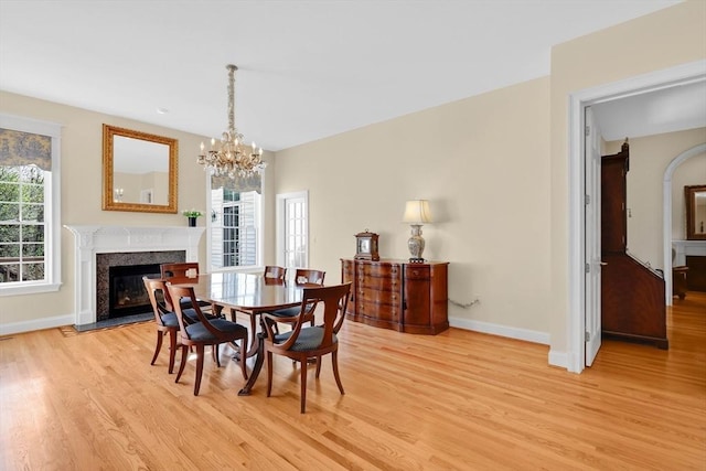 dining area featuring baseboards, light wood finished floors, a notable chandelier, and a premium fireplace
