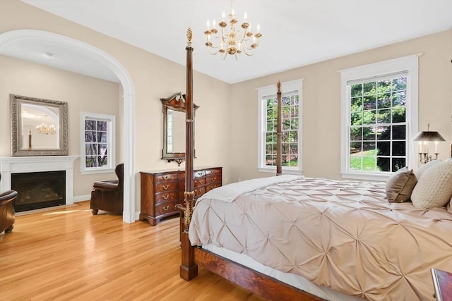 bedroom featuring light wood-style floors, a fireplace with flush hearth, arched walkways, and a notable chandelier