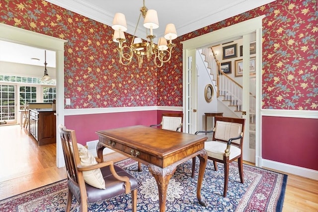 dining room featuring stairs, wood finished floors, wallpapered walls, a wainscoted wall, and a notable chandelier