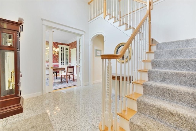 staircase with crown molding, arched walkways, speckled floor, baseboards, and a towering ceiling