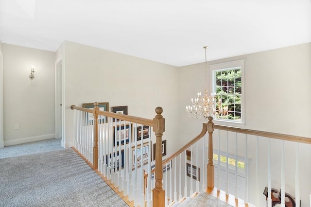 hall with carpet flooring, baseboards, an upstairs landing, and an inviting chandelier