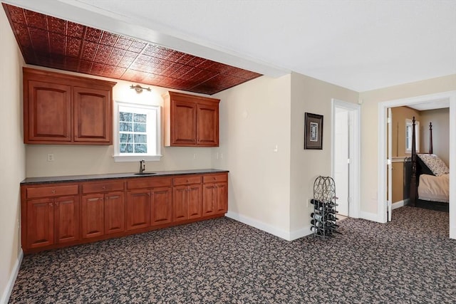 kitchen with baseboards, carpet flooring, brown cabinetry, and dark countertops