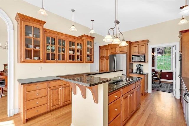 kitchen featuring brown cabinets, a center island, stainless steel appliances, light wood-type flooring, and glass insert cabinets