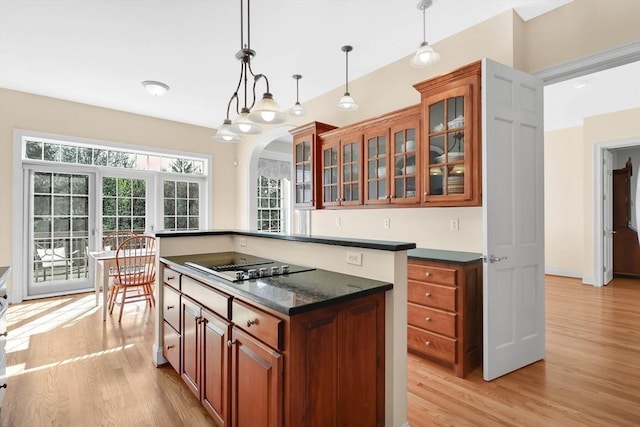kitchen with light wood-style floors, black electric cooktop, brown cabinetry, decorative light fixtures, and glass insert cabinets