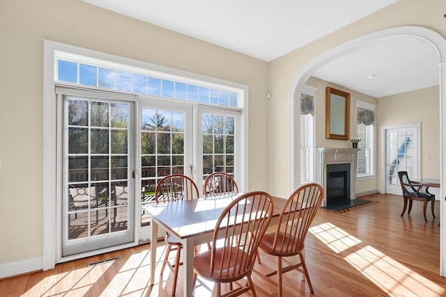 dining space featuring arched walkways, baseboards, a glass covered fireplace, and light wood-style flooring