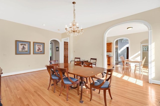 dining room with baseboards, arched walkways, light wood-style flooring, and a notable chandelier