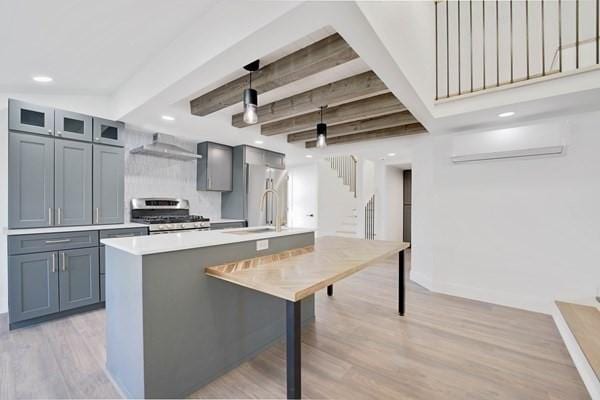 kitchen with stainless steel range oven, decorative light fixtures, a center island with sink, beamed ceiling, and range hood