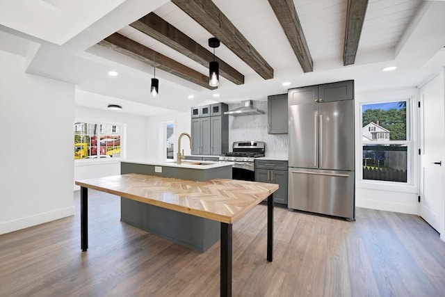 kitchen featuring appliances with stainless steel finishes, sink, decorative backsplash, hanging light fixtures, and wall chimney exhaust hood