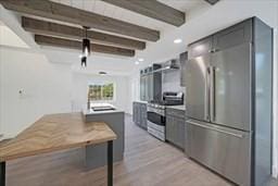 kitchen featuring beamed ceiling, appliances with stainless steel finishes, and light hardwood / wood-style flooring