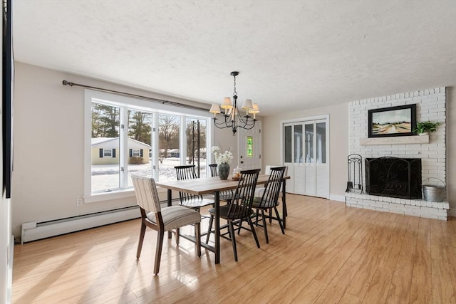 dining space featuring a baseboard heating unit, a textured ceiling, a brick fireplace, and light wood-style flooring