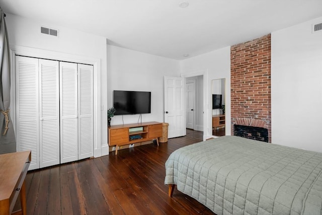 bedroom with a closet, hardwood / wood-style flooring, a brick fireplace, and visible vents