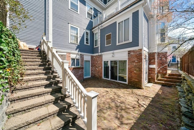 back of house with stairway, brick siding, and a patio area