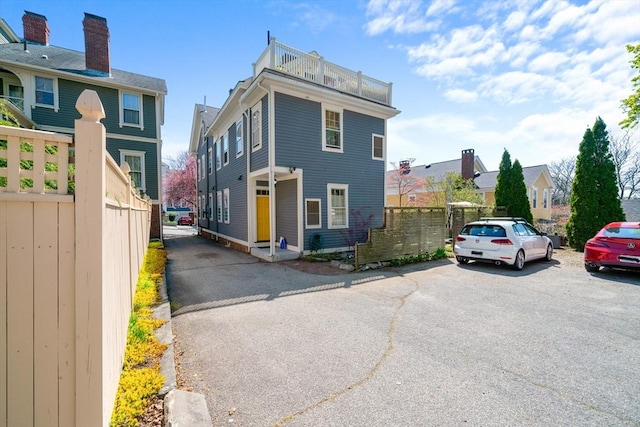 exterior space featuring uncovered parking, fence, a balcony, and a residential view