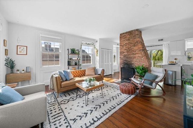 living area with a brick fireplace, wood finished floors, and visible vents