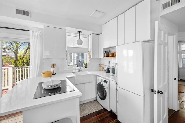 kitchen featuring washer / dryer, freestanding refrigerator, black electric stovetop, and visible vents
