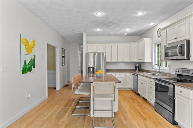 8 Mill River Ln, Rowley, MA 01969 - kitchen with appliances with stainless steel finishes, white cabinets, light wood-style flooring, a center island, and a kitchen bar