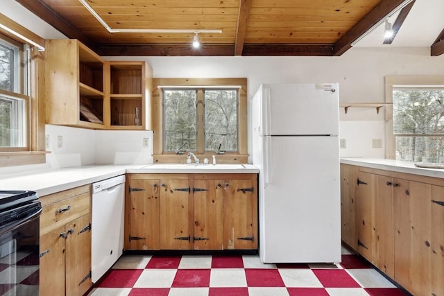 kitchen with a sink, white appliances, beam ceiling, and light floors