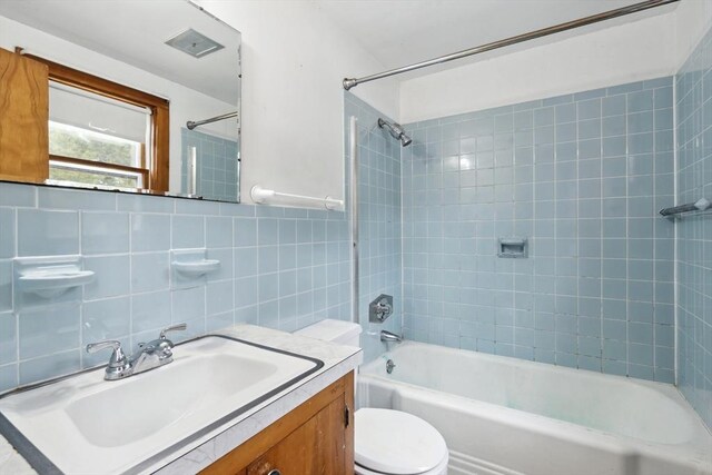 bathroom featuring shower / bathing tub combination, tile walls, toilet, and vanity