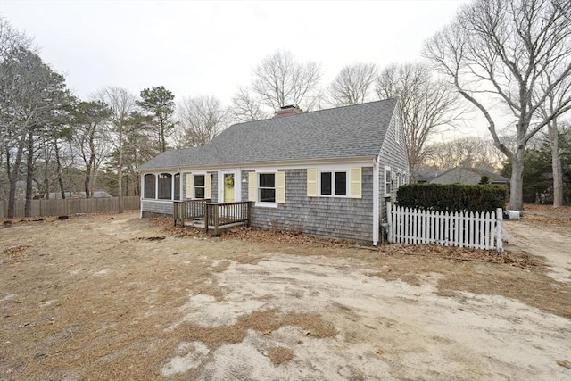 view of front of home with a sunroom, a shingled roof, a chimney, and fence