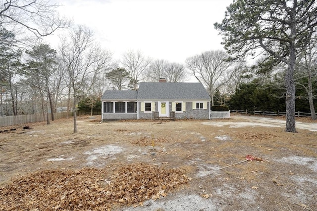 view of front of house featuring roof with shingles, a chimney, fence, and a sunroom