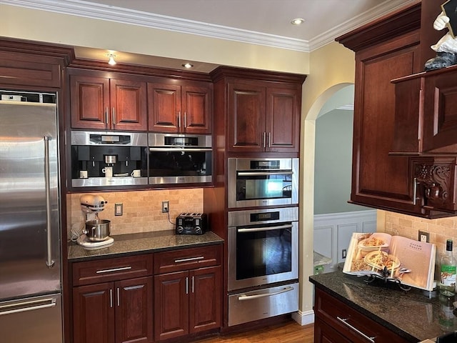 kitchen with tasteful backsplash, crown molding, arched walkways, stainless steel appliances, and a warming drawer