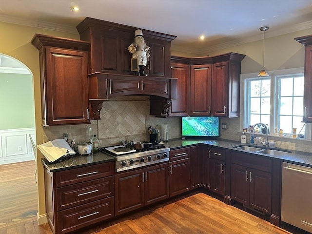 kitchen featuring decorative light fixtures, ornamental molding, appliances with stainless steel finishes, wood finished floors, and a sink