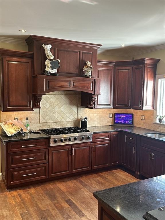 kitchen with a sink, backsplash, dark wood-style floors, stainless steel gas stovetop, and crown molding