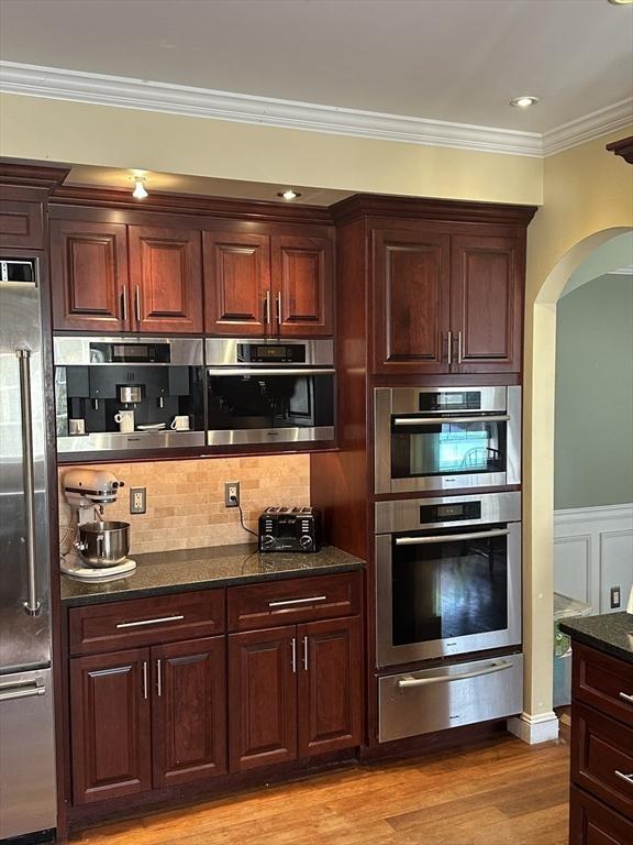 kitchen featuring light wood finished floors, stainless steel appliances, decorative backsplash, crown molding, and a warming drawer