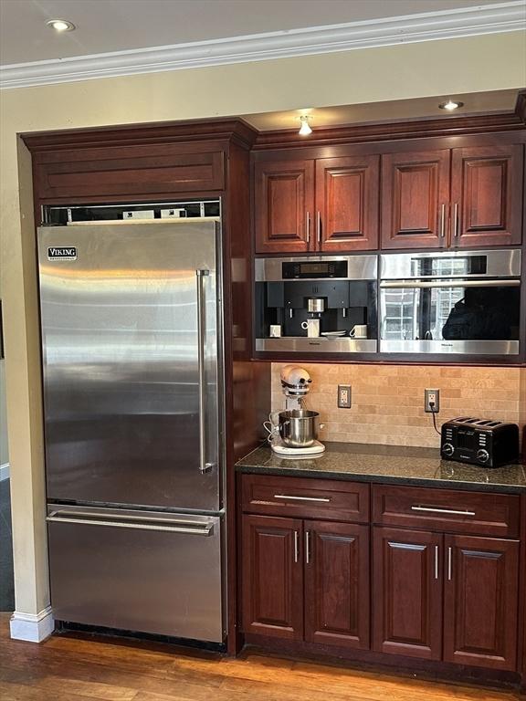 kitchen featuring light wood finished floors, stainless steel appliances, crown molding, a toaster, and decorative backsplash