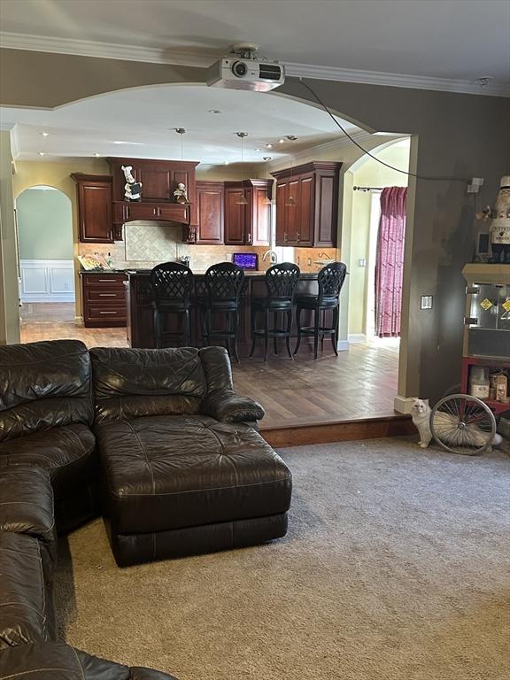 carpeted living room with arched walkways and ornamental molding