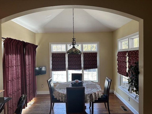 dining area featuring arched walkways, baseboards, lofted ceiling, and dark wood-style flooring