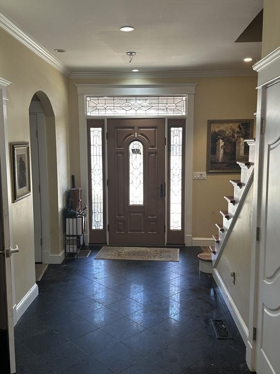 entrance foyer featuring arched walkways, stairway, baseboards, and ornamental molding