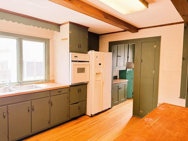 kitchen with light wood-style floors, white appliances, light countertops, a sink, and beam ceiling