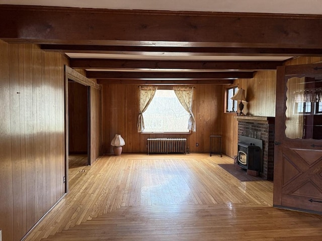 unfurnished living room with wooden walls, light wood-type flooring, radiator, and beam ceiling