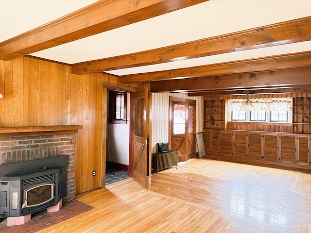 unfurnished living room featuring wooden walls, radiator heating unit, a wood stove, light wood-style floors, and beamed ceiling