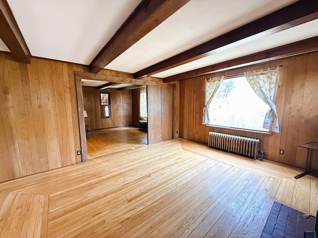 interior space featuring a healthy amount of sunlight, wooden walls, beam ceiling, radiator, and wood-type flooring