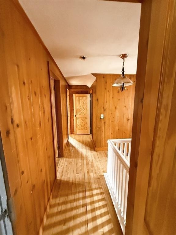 corridor with wooden walls, baseboards, hardwood / wood-style floors, and an upstairs landing
