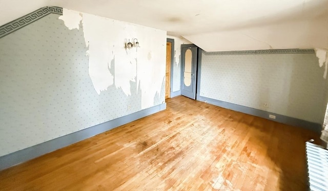 bonus room featuring baseboards, vaulted ceiling, wood finished floors, and wallpapered walls