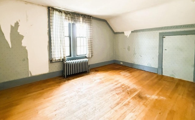 bonus room featuring wallpapered walls, radiator heating unit, wood finished floors, and lofted ceiling