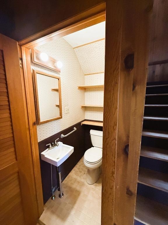 half bath featuring vaulted ceiling, toilet, a sink, tile patterned floors, and wallpapered walls