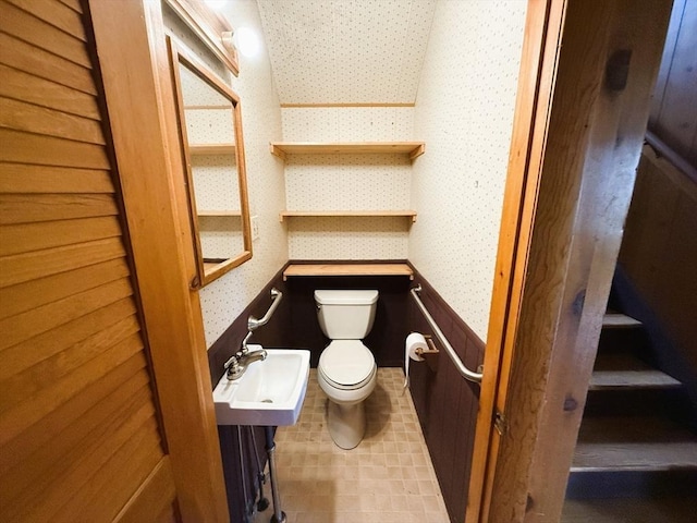 half bathroom featuring a sink, toilet, and wallpapered walls