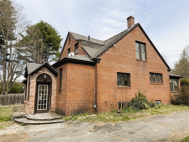 view of side of home featuring roof with shingles, a chimney, fence, and brick siding