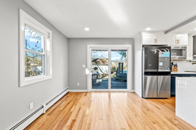 kitchen with white cabinets, light hardwood / wood-style floors, baseboard heating, and appliances with stainless steel finishes