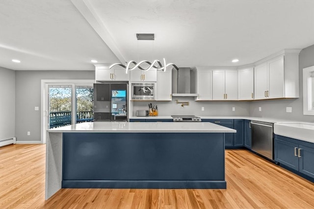 kitchen with stainless steel appliances, blue cabinets, wall chimney range hood, decorative light fixtures, and white cabinetry