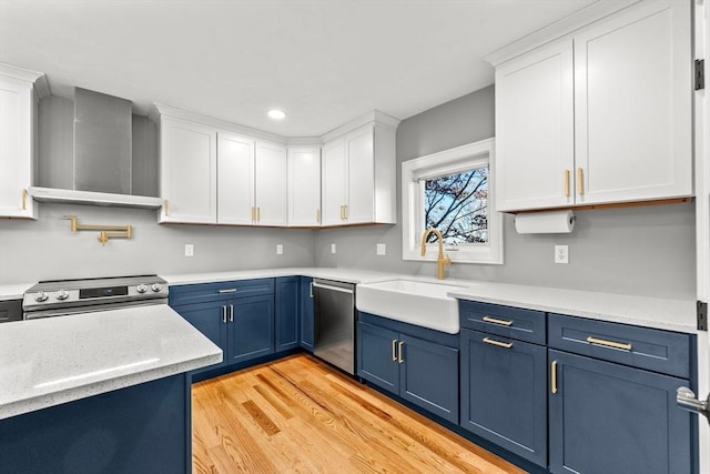 kitchen with sink, stainless steel appliances, wall chimney range hood, white cabinets, and light wood-type flooring