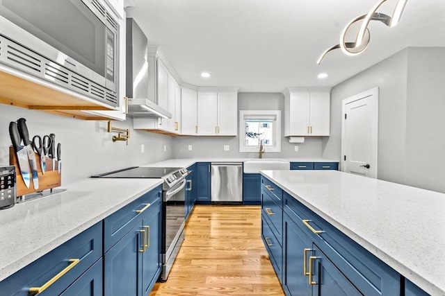 kitchen featuring white cabinets, blue cabinets, wall chimney exhaust hood, light stone counters, and stainless steel appliances