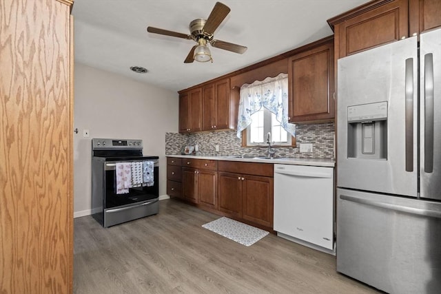 kitchen with sink, tasteful backsplash, light hardwood / wood-style flooring, ceiling fan, and stainless steel appliances