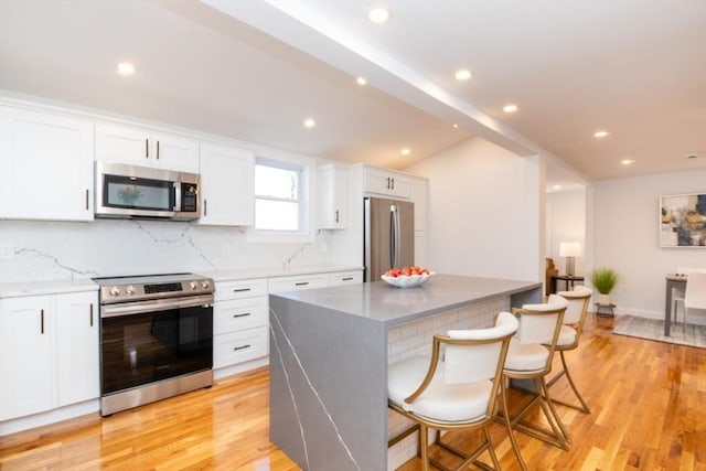 kitchen featuring tasteful backsplash, white cabinets, light wood-style flooring, a center island, and stainless steel appliances