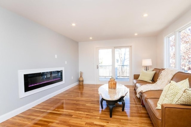 living area featuring light wood-type flooring, a glass covered fireplace, baseboards, and recessed lighting