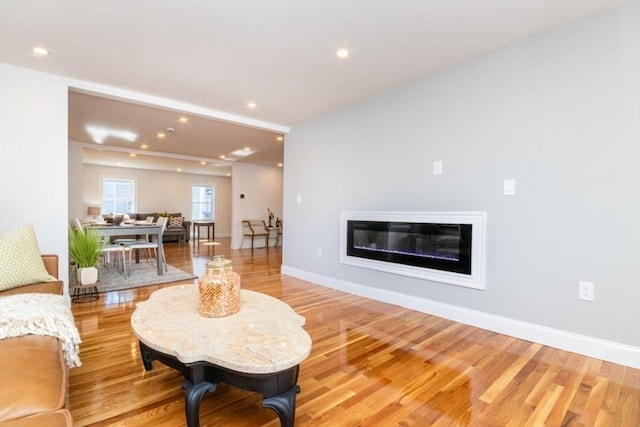 living room with recessed lighting, light wood-style flooring, baseboards, and a glass covered fireplace